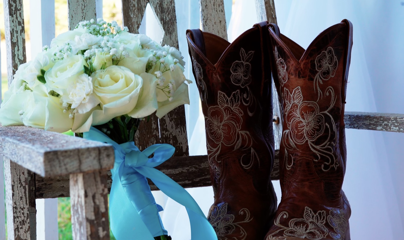 Bridal bouquet and cowboy boots arranged beside the wedding dress