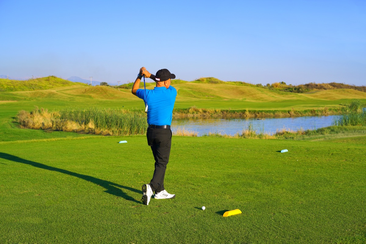 A golfer mid-swing on a green fairway