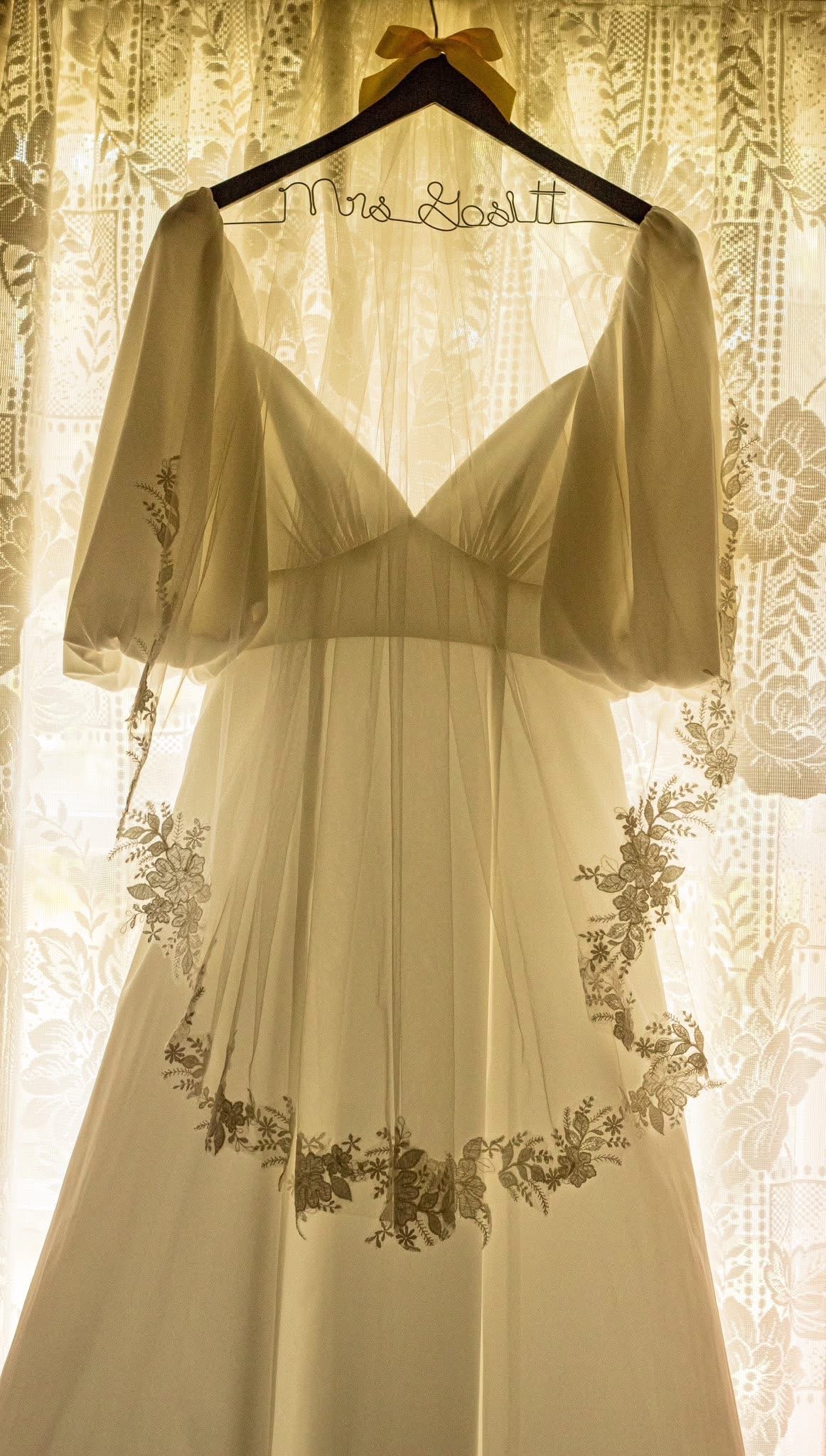 Wedding dress hanging in warm window light before the ceremony